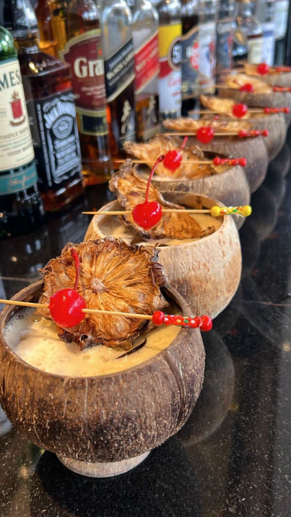 Coconut shells filled with Piña colada,  garnished with dehydrated pineapples and cherries on a bar counter.