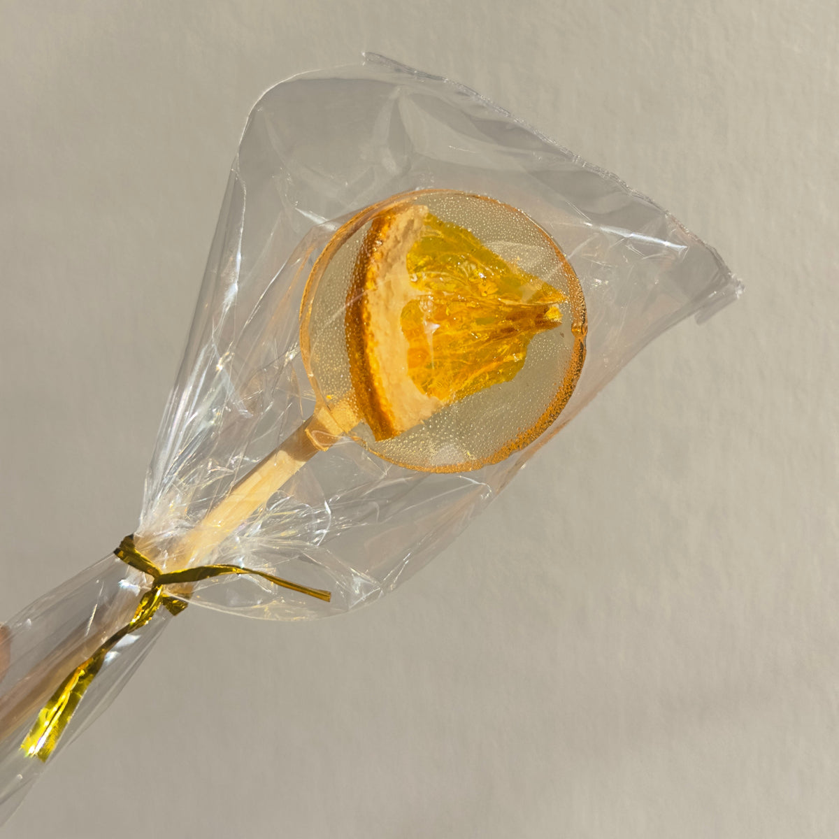 Lollipop with orange slice on a clear stick, wrapped in cellophane against a neutral background