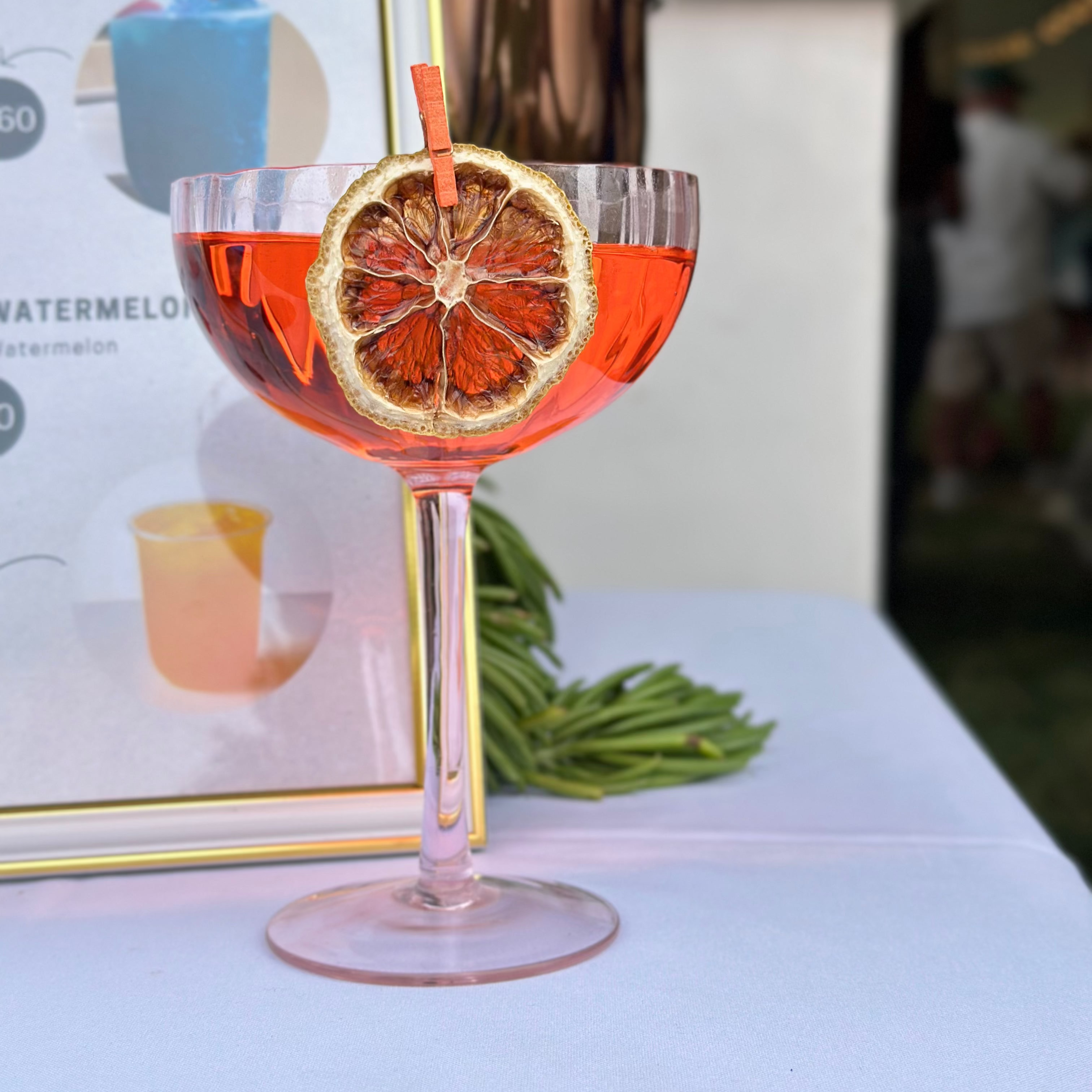 Cocktail glass with pink liquid, dried orange slice, and straw on a white surface.